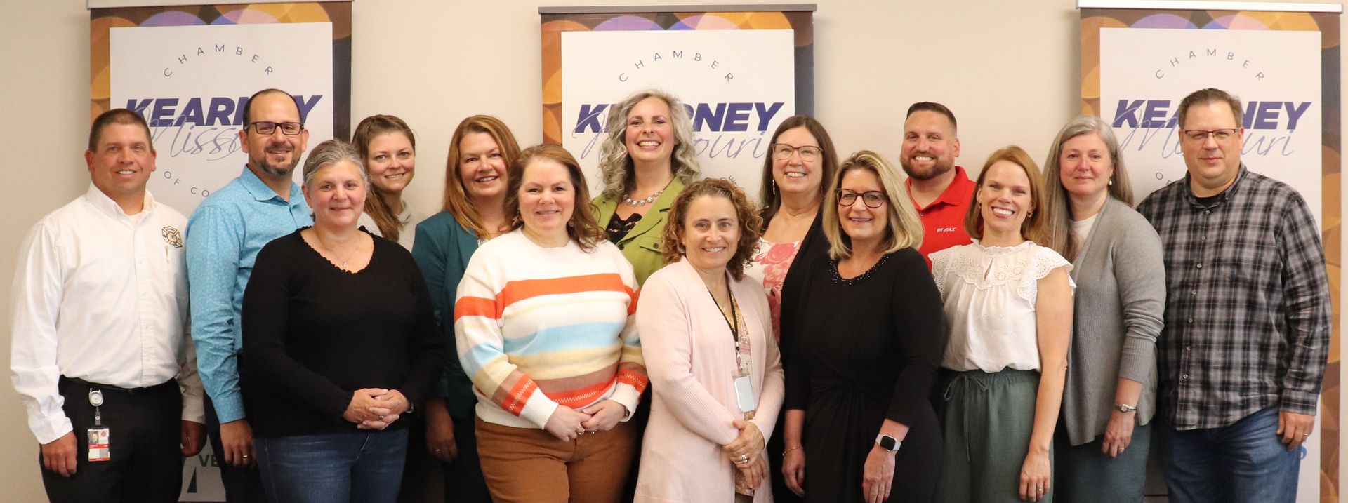 A group of people poses for a photo in an office setting. They are standing in front of a banner.