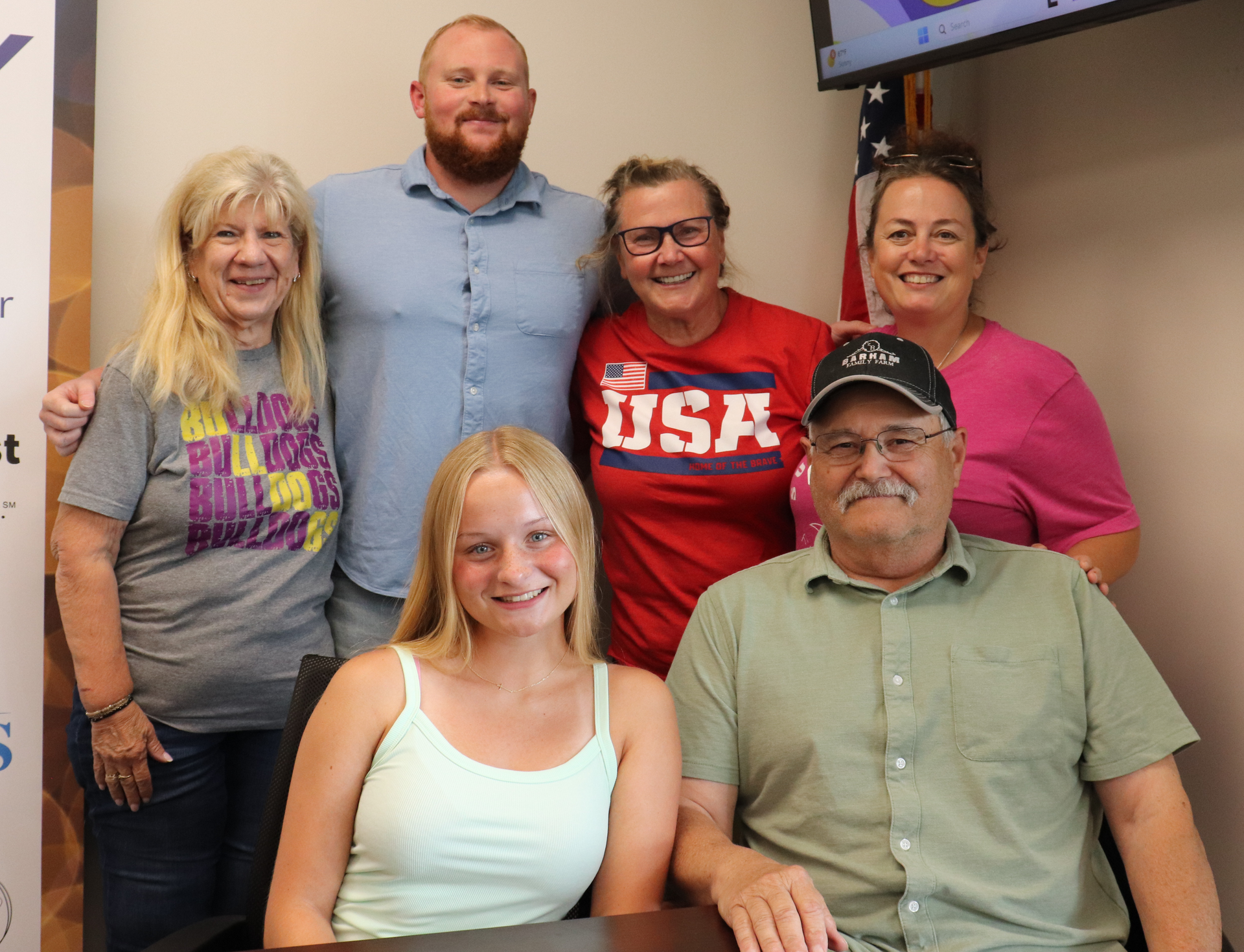 A group of six people posing for a photo indoors; they are diverse in age and appear happy and friendly.