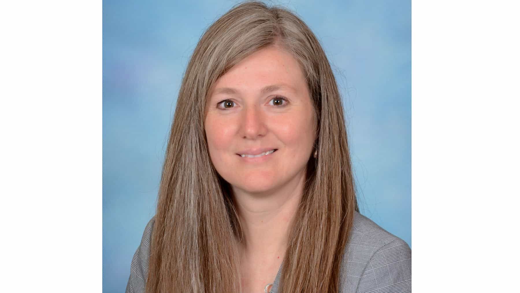 Woman with long, graying hair, smiling and looking at the camera. She is wearing a striped shirt against a blue background.