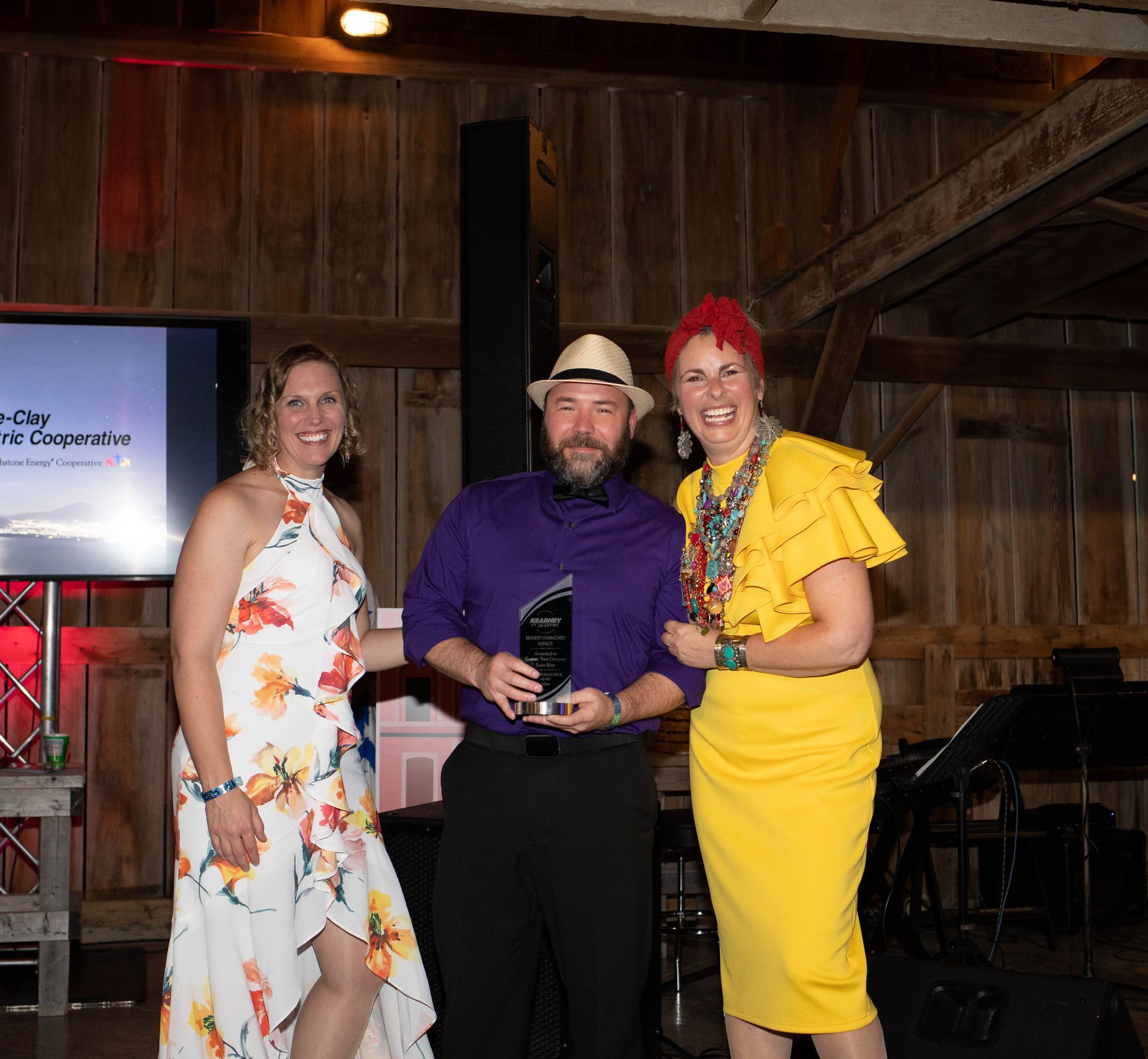 Three people smiling and holding an award in a barn-like setting. A man in a hat holds the award, flanked by two women.