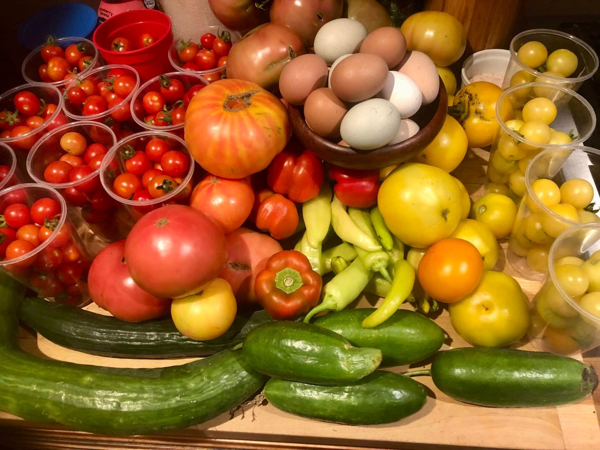 Colorful assortment of freshly harvested vegetables, including tomatoes, peppers, cucumbers, and eggs, displayed on a wooden surface.