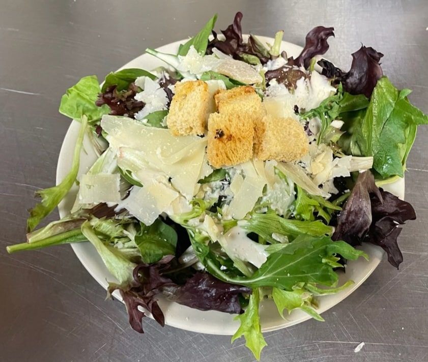 Salad with mixed greens, Parmesan cheese, croutons, and dressing in a white bowl.