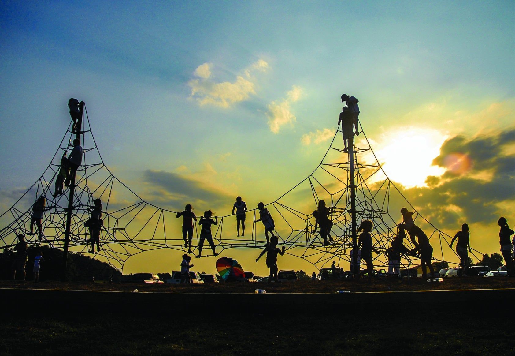 Children playing on a climbing net structure silhouetted against a sunset sky.