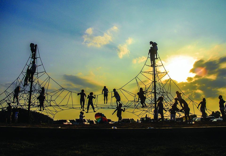 Children playing on a climbing net structure silhouetted against a sunset sky.