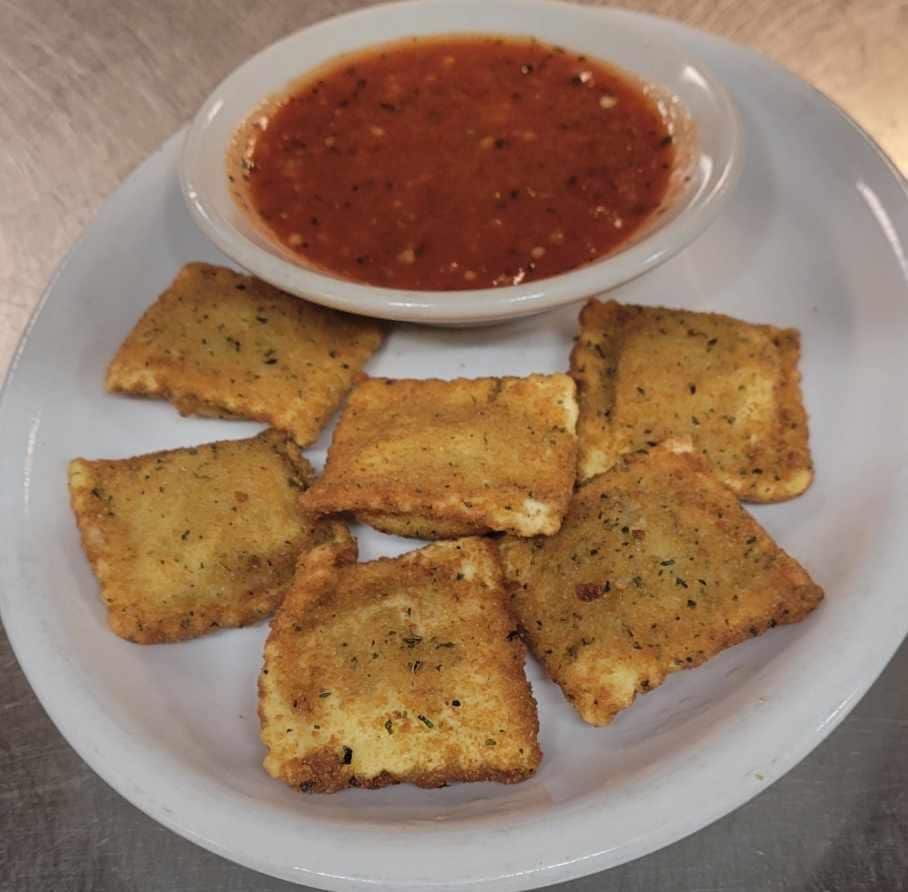 Fried ravioli on a plate with a bowl of red marinara sauce for dipping.