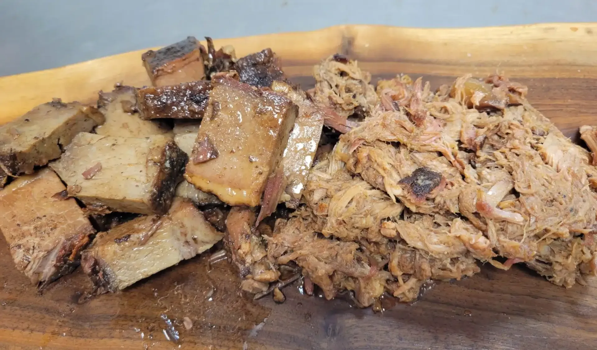 Chopped and shredded cooked beef on a wooden cutting board, with dark brown and charred appearance.