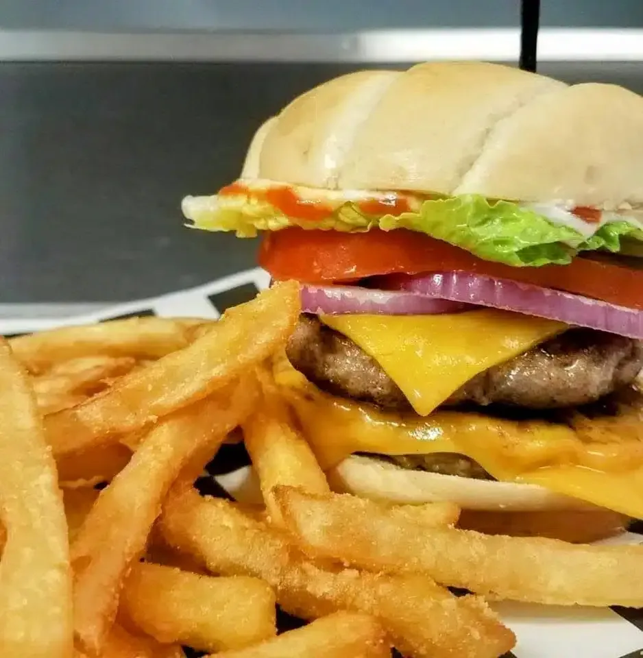 Double cheeseburger with lettuce, tomato, and red onion on a white bun, with fries. Served on a checkered paper.