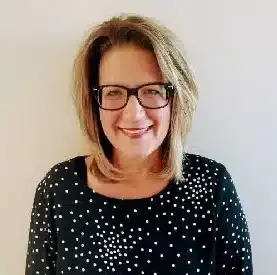 Woman with glasses wearing a black top with white polka dots, smiling.