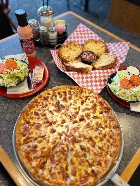 A pizza, salads, and garlic bread on a table at a restaurant.