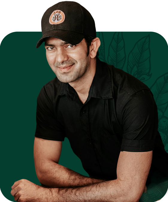Man in black cap and shirt, smiling, leaning on a dark green background.