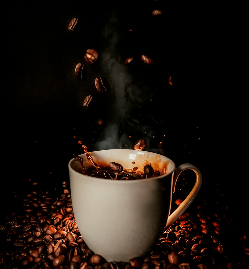 White coffee cup with gold handle, coffee beans falling in with steam rising.