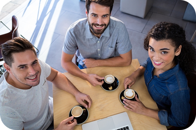 Three smiling friends enjoying coffee together at a cafe table.