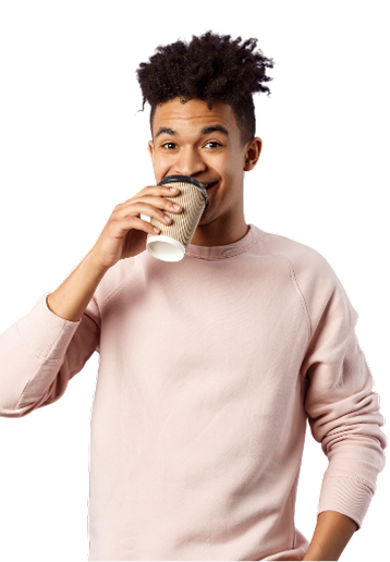 Young man with curly hair sipping coffee, wearing a pink sweater, smiling.