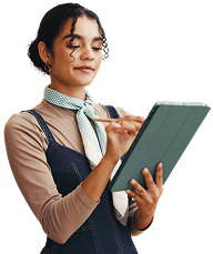Woman in denim dress using a stylus on a tablet, smiling. White background.