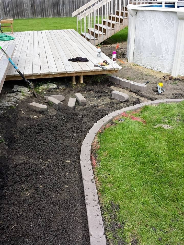 Backyard landscaping project with deck, grass, and brick edging.