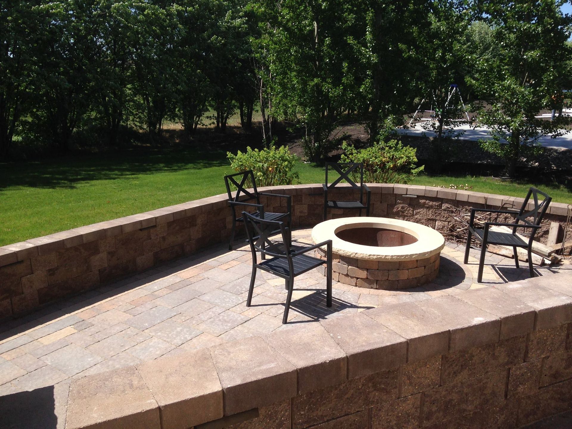 Patio with a fire pit and four chairs, surrounded by brick walls and green grass.