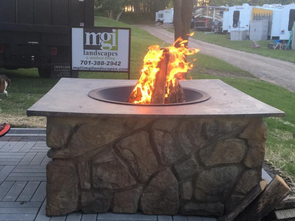 Fire pit with large flames. Stone base and concrete top. Outdoor setting with RVs in the background.