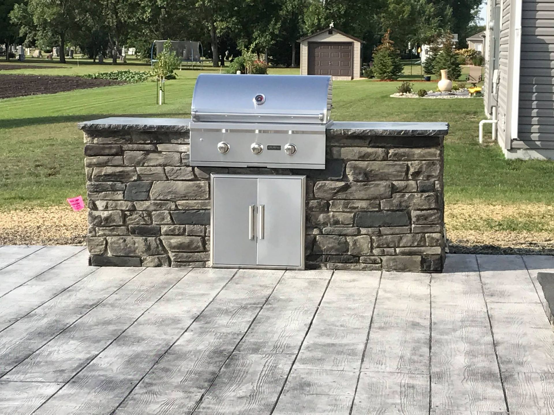 Outdoor kitchen with stainless steel grill, stone facade, and gray patio.