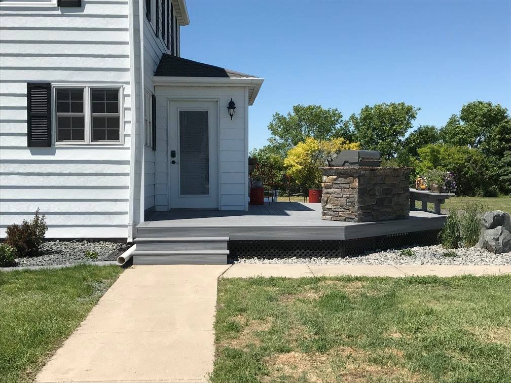 White house with gray composite deck and stone feature. Pathway to front door on sunny day.