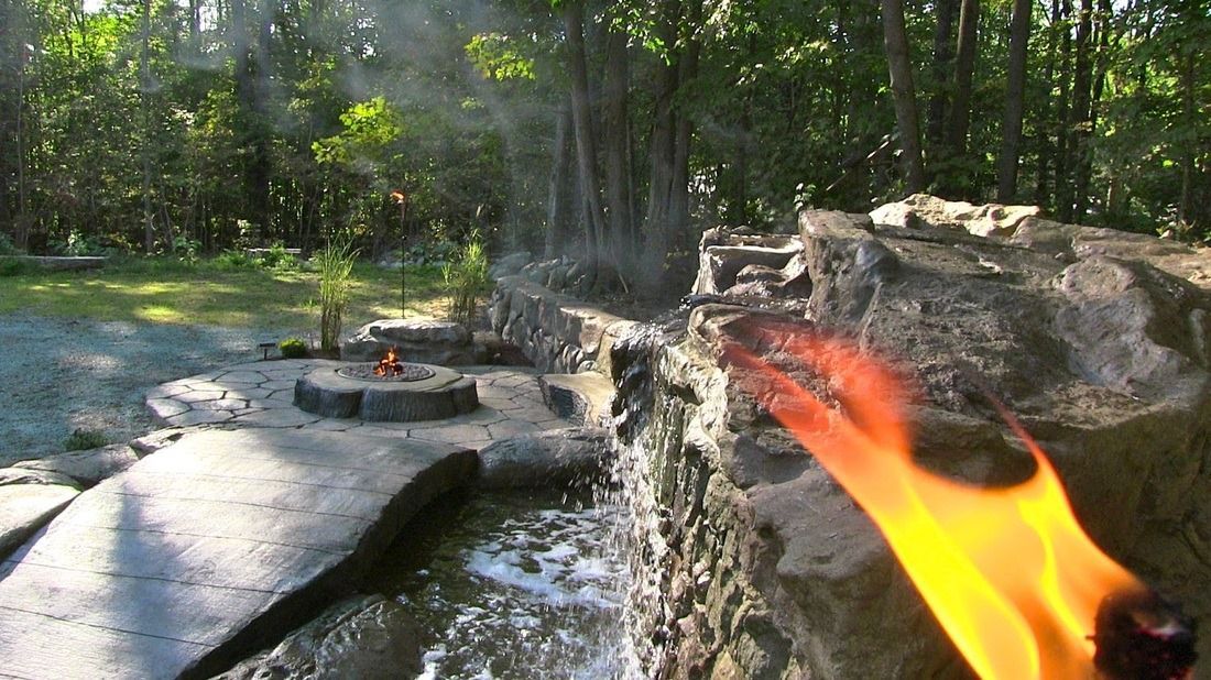 Torch lit foreground, small fire, rocky ledge and trees in a tropical setting.