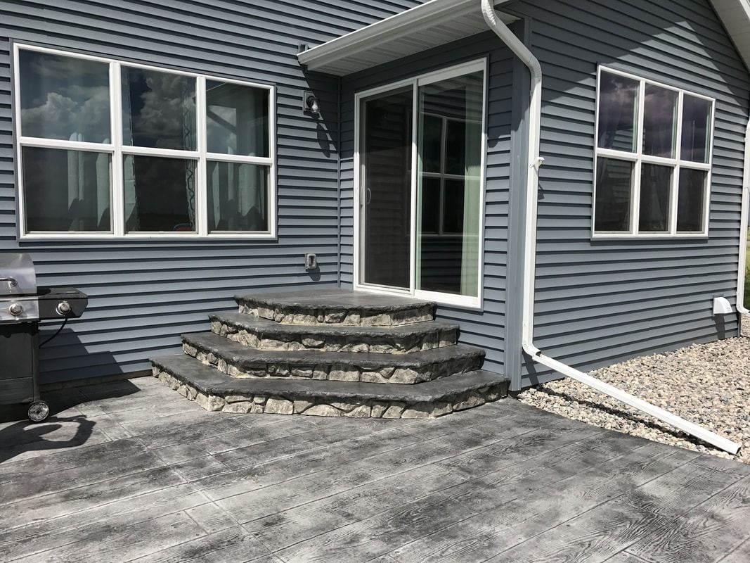 Exterior view of a house with grey siding, patio, and steps leading to a sliding door.