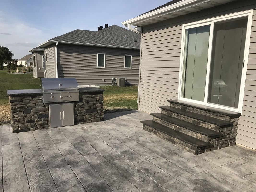 Outdoor patio with built-in grill and steps up to a sliding door on a house.