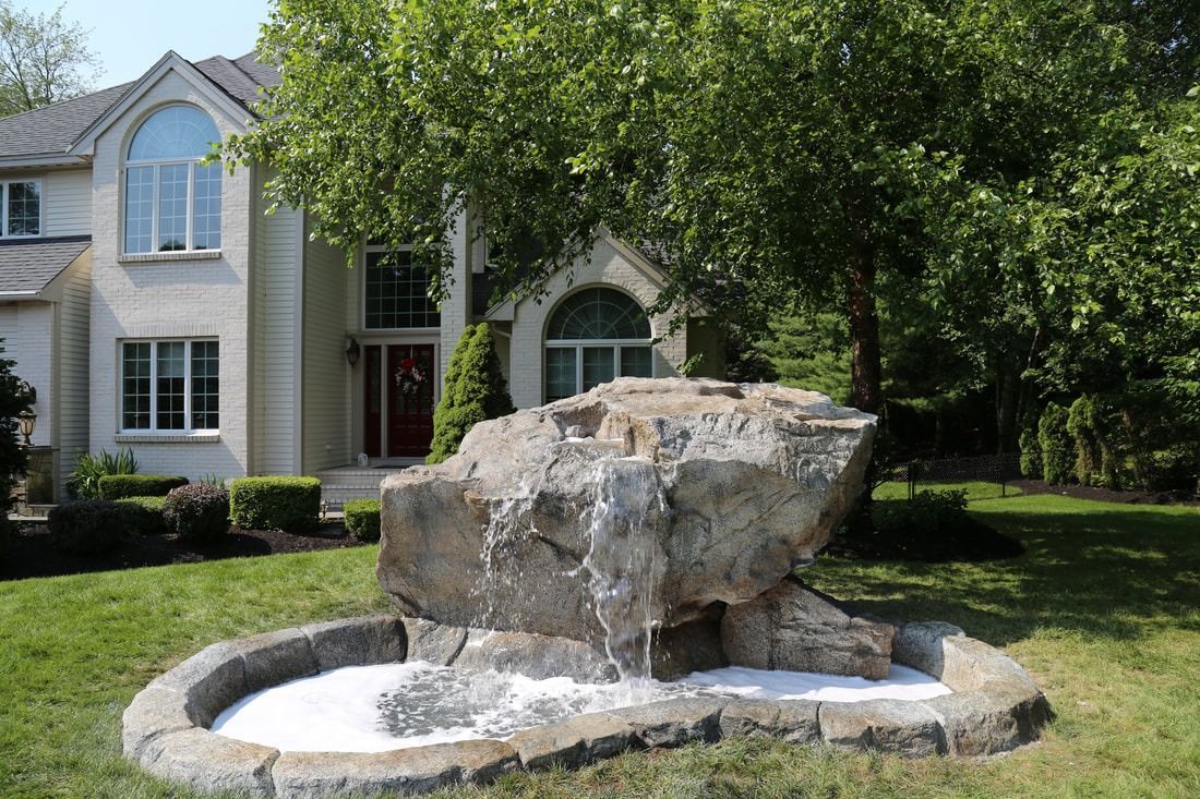 Stone waterfall feature in front of a large white house with arched windows and green lawn.