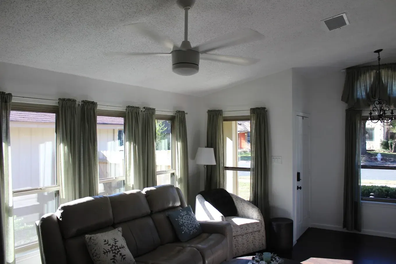 Living room with sofa, windows, ceiling fan, and green curtains.