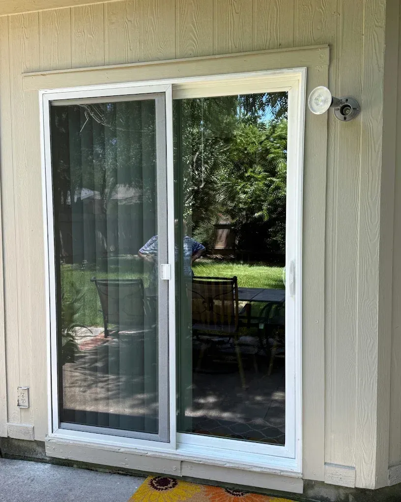 Sliding glass door with a white frame and screen. Exterior view with trees and patio furniture visible.