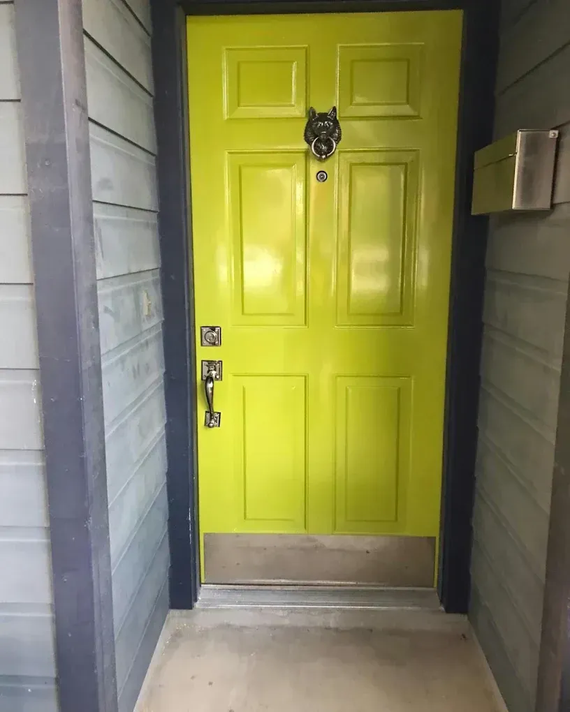 Bright lime-green door with black trim and silver door knocker in a doorway framed by gray siding.