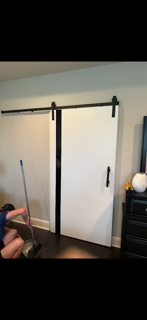 Person sweeping near white barn doors. Black hardware, dark wood floor.