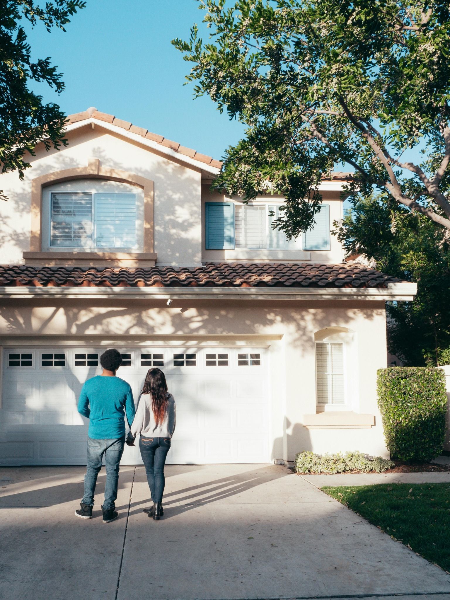 Couple walking towards a two-story house with a white garage door; sunny day.