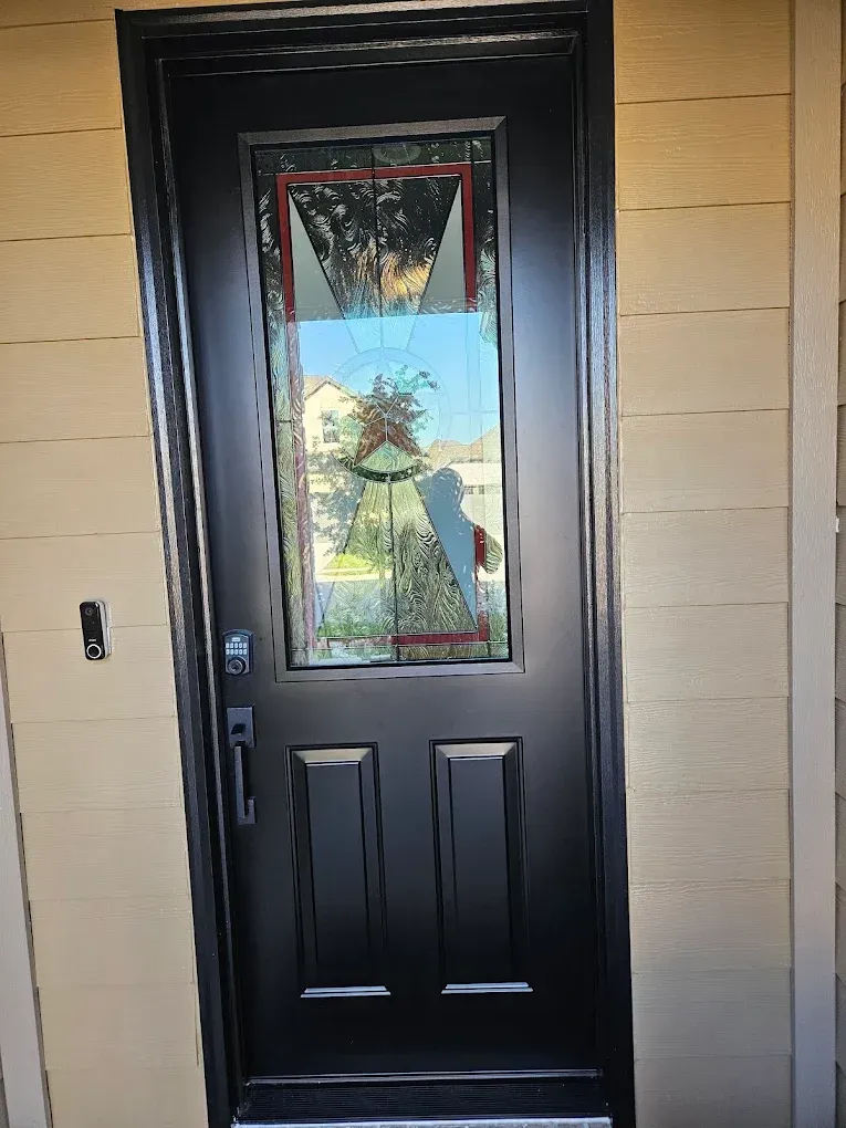 Black front door with glass panel, holiday decorations visible, beige siding.