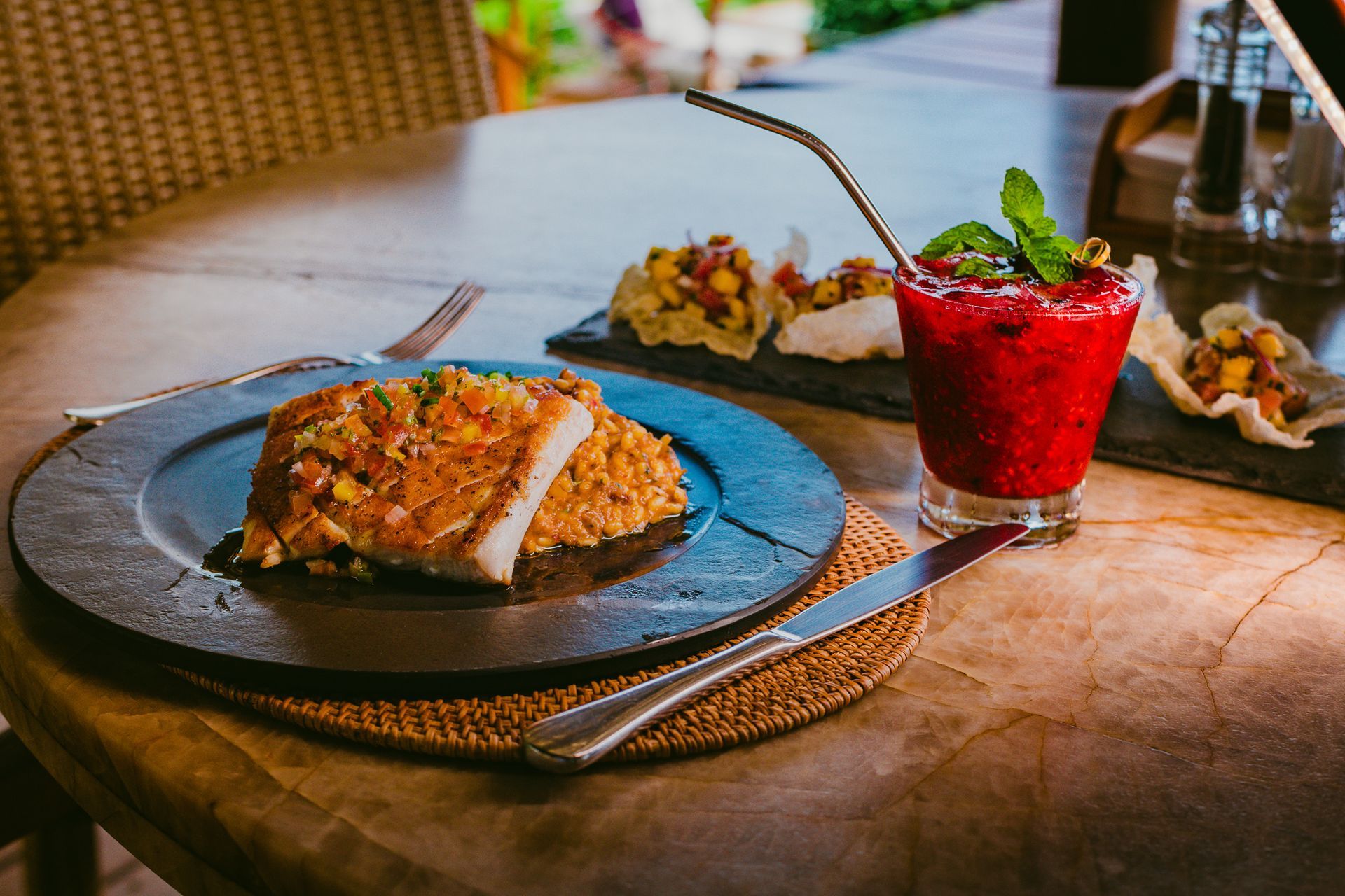 Refeição na mesa: Costeleta de porco e acompanhamento em um prato, smoothie de frutas vermelhas e aperitivos, ambiente externo.