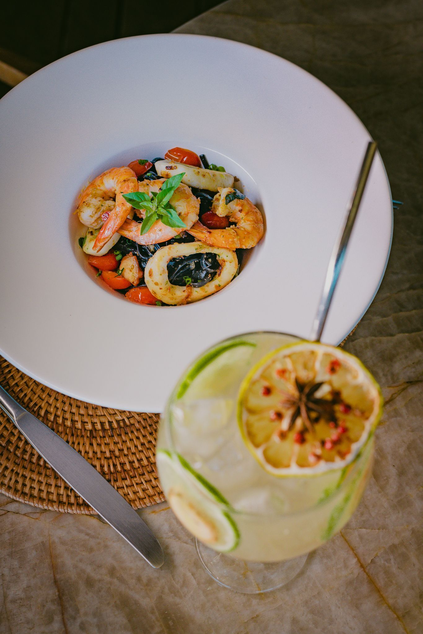Macarrão com frutos do mar, camarão e tomate em uma tigela branca, além de um coquetel de limão.