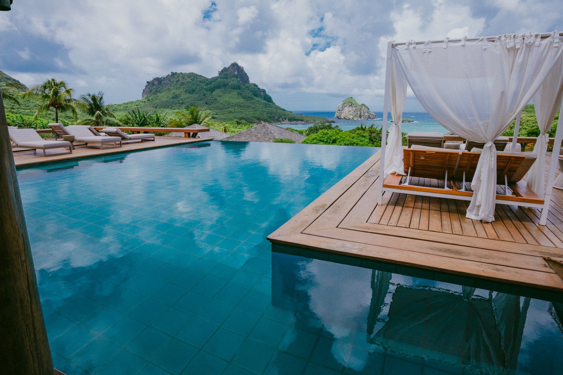 Piscina de borda infinita com deck de madeira, cabana e vista para o mar com vista para o pico da ilha.
