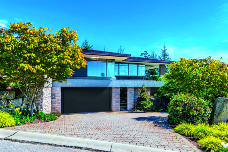Una grande casa con la porta del garage nera e il vialetto di mattoni.