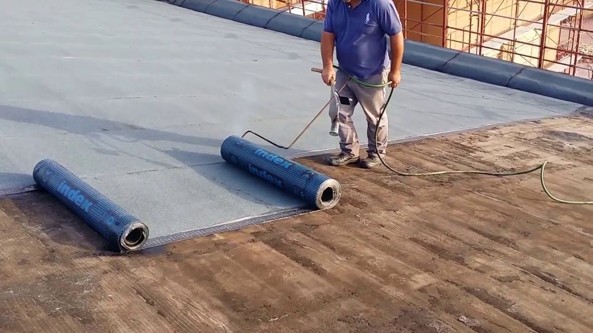 Un uomo è in piedi su un tetto con due rotoli di materiale di copertura.