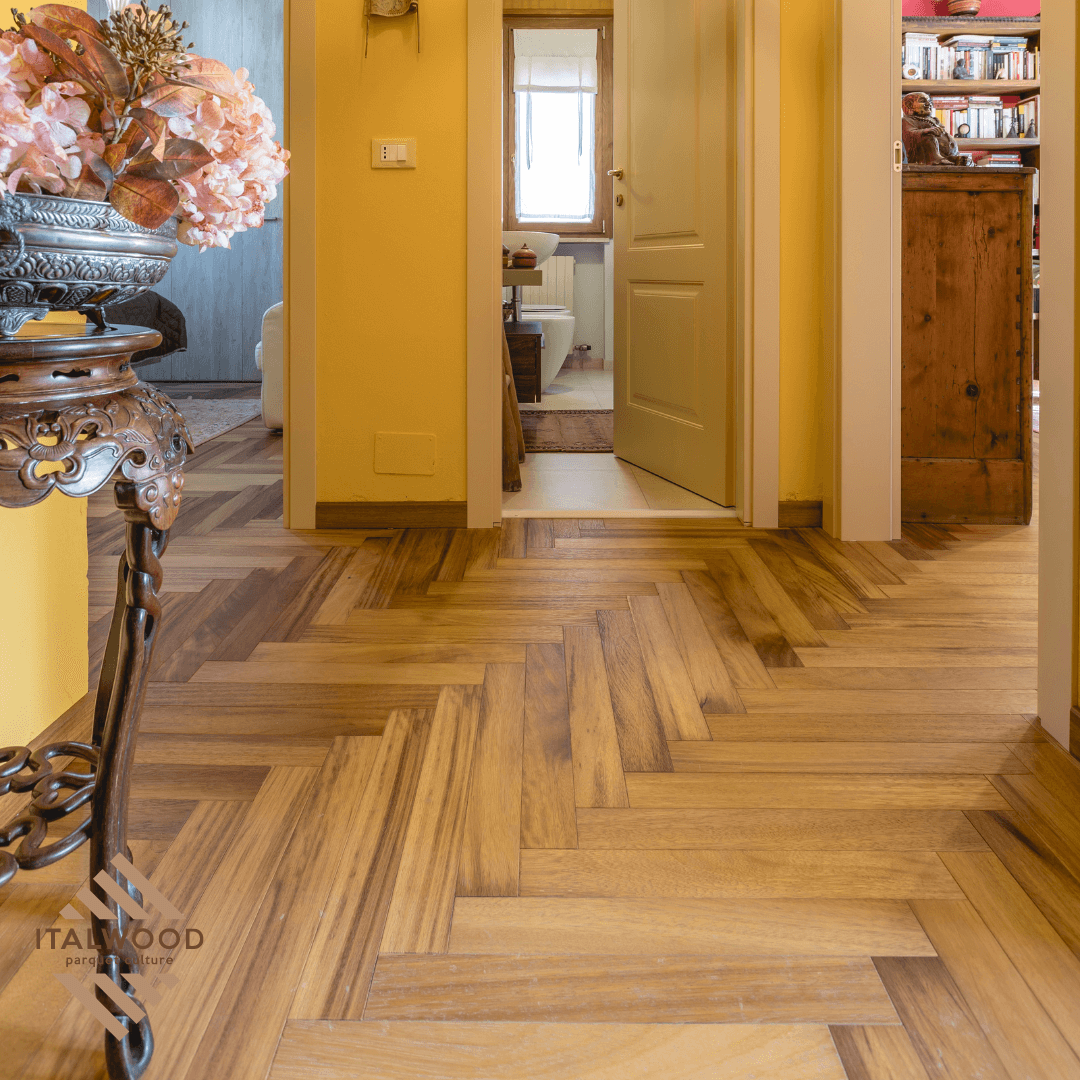 Un corridoio con pavimento in legno e un vaso di fiori su un tavolo.