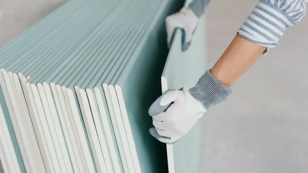 Una persona tiene in mano una pila di fogli di cartongesso.