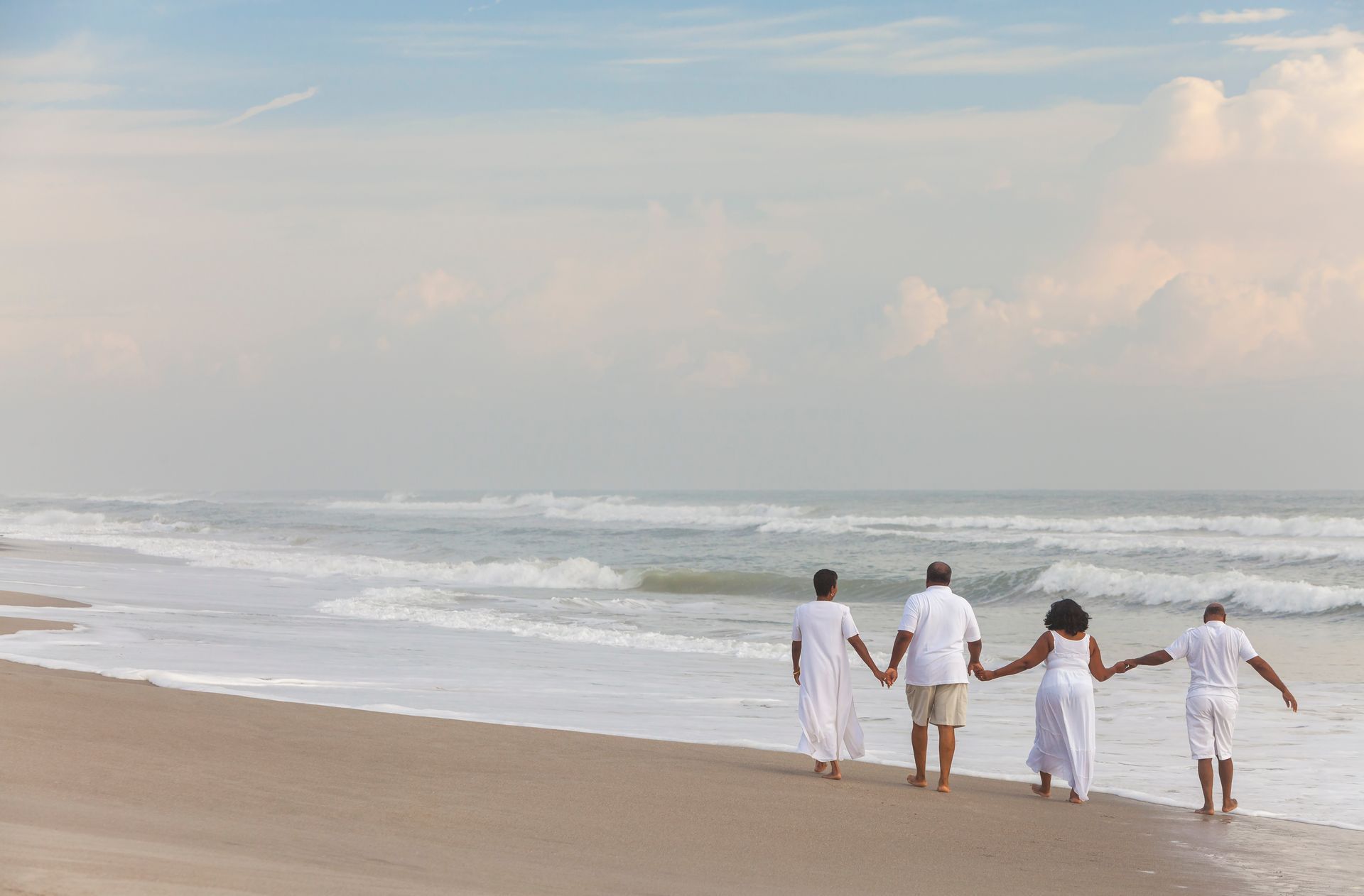 a family is walking on the beach holding hands .