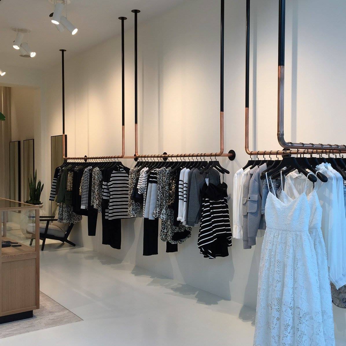 Clothing store with clothing racks made of copper pipes, hanging clothes in a minimalist setting.