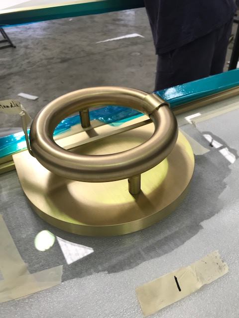 Brass circular handle on a round brass base, possibly a door pull. Blue and white background.