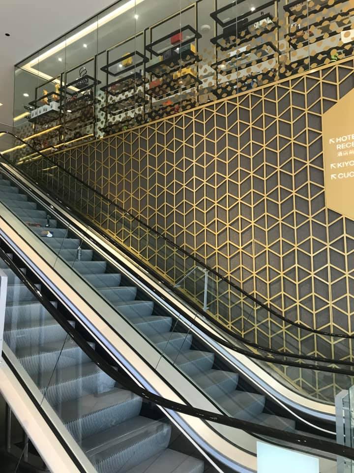 Escalator ascending past gold geometric wall, shelves of merchandise.