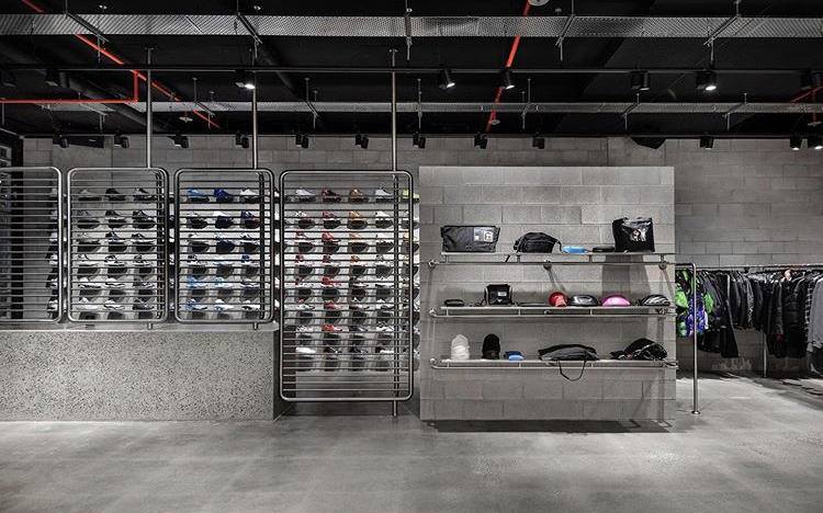 Interior of a retail store with metal shelving displaying shoes and accessories. Gray walls and flooring.