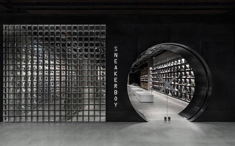 Black storefront with a glass block wall and circular doorway leading into a sneaker store. 