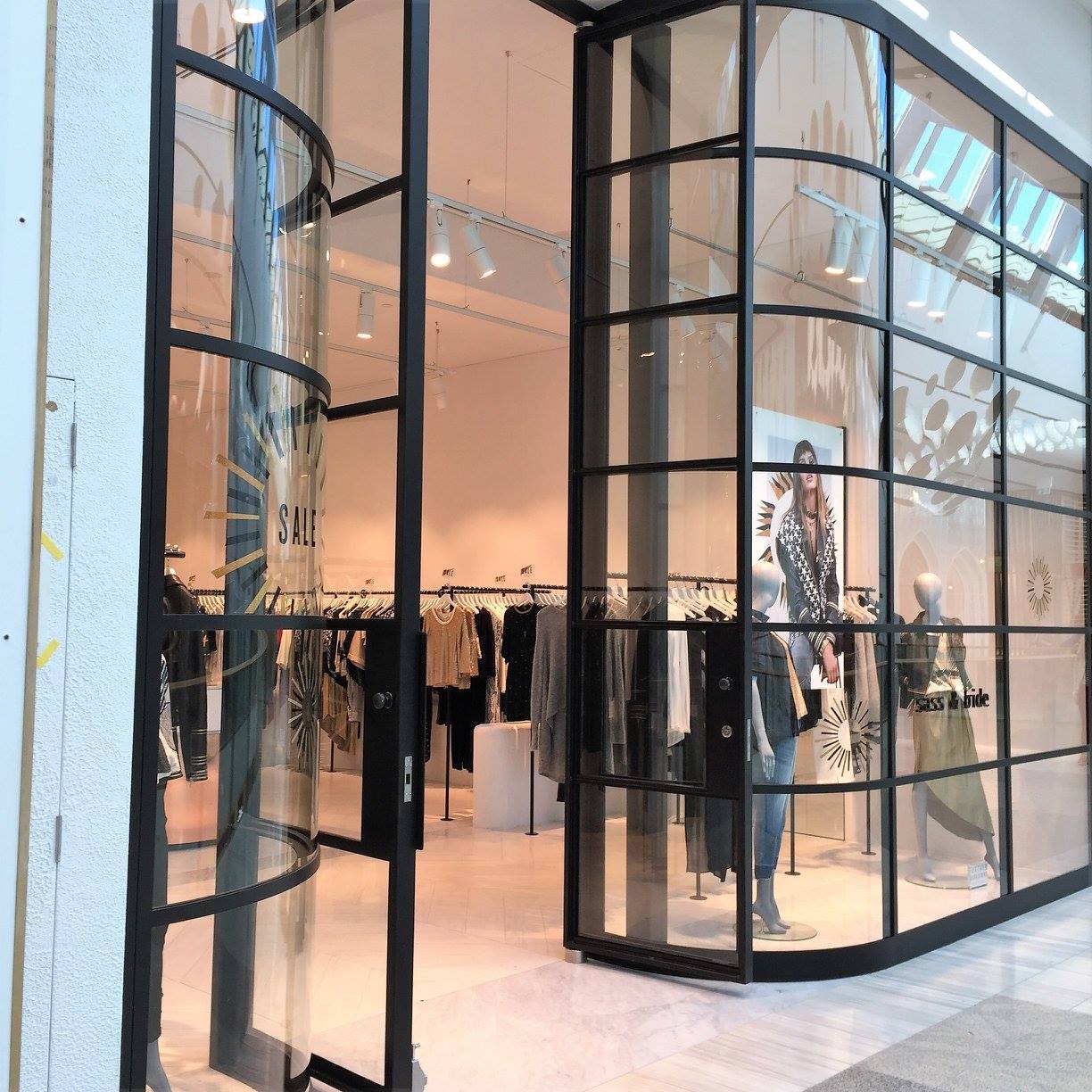 Black framed glass storefront with curved corner, clothes racks visible inside.