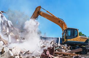 A large yellow excavator is demolishing a building.