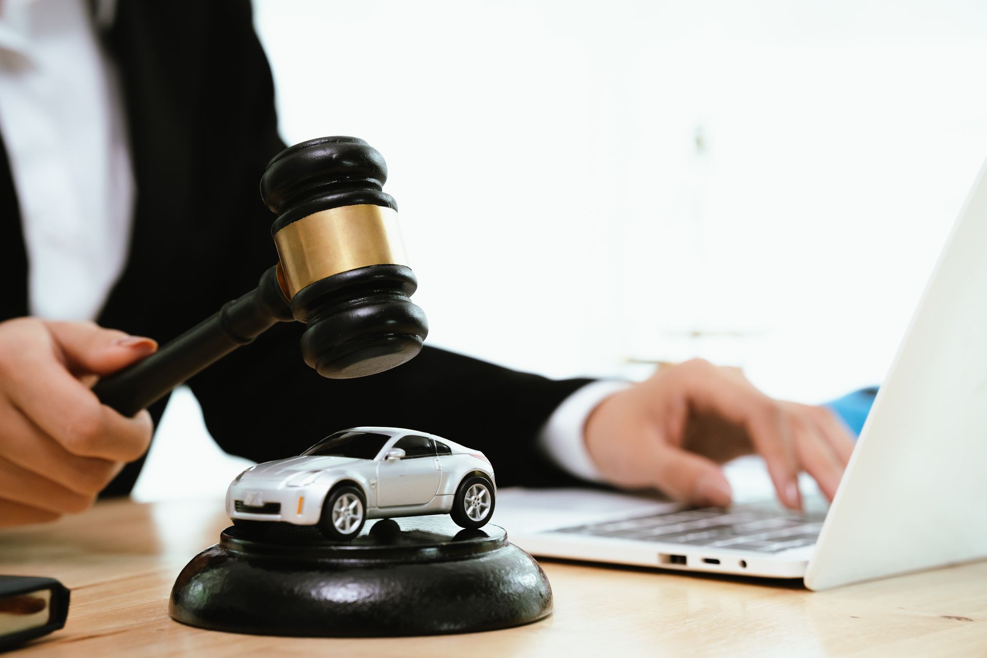 A lawyer in a suit uses a gavel near a toy car on a wooden base, symbolizing car accident cases. A lawyer in a suit uses a gavel near a toy car on a wooden base, symbolizing car accident cases.