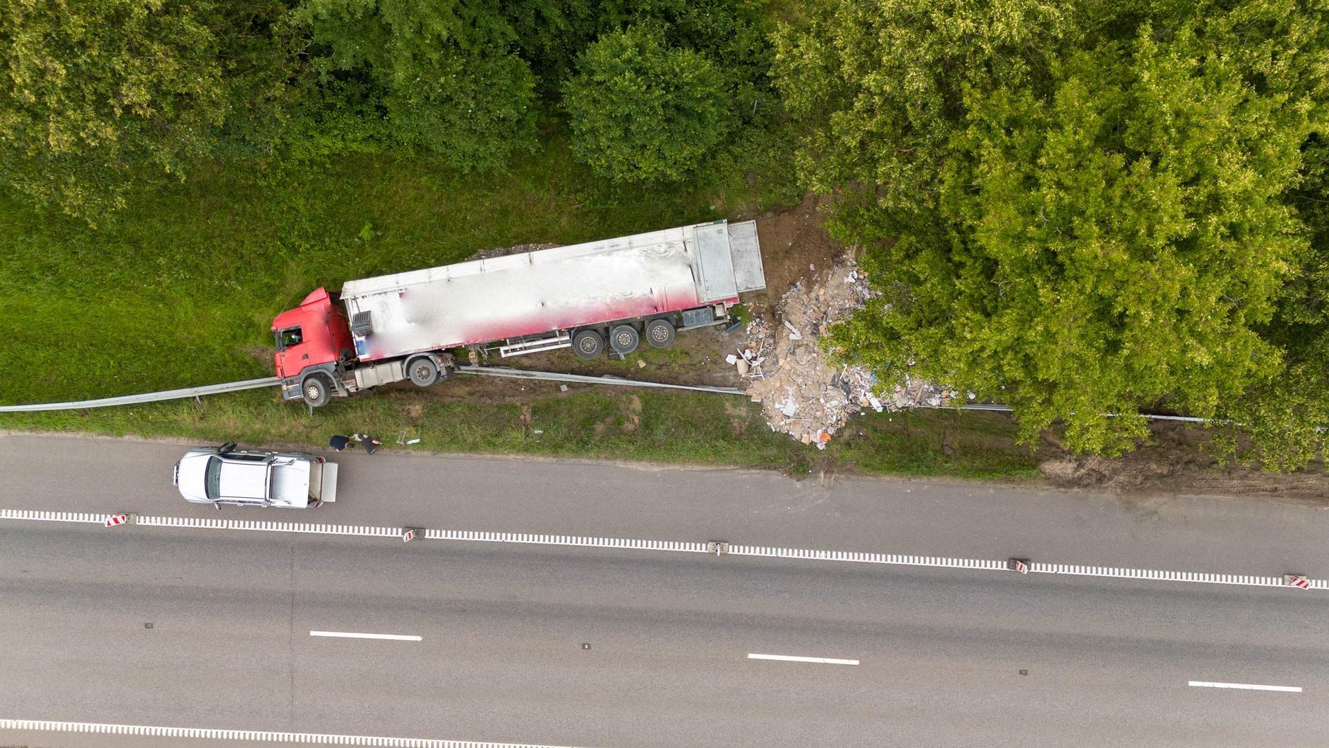 An aerial view of a red truck off the road, with debris scattered nearby after an accident.